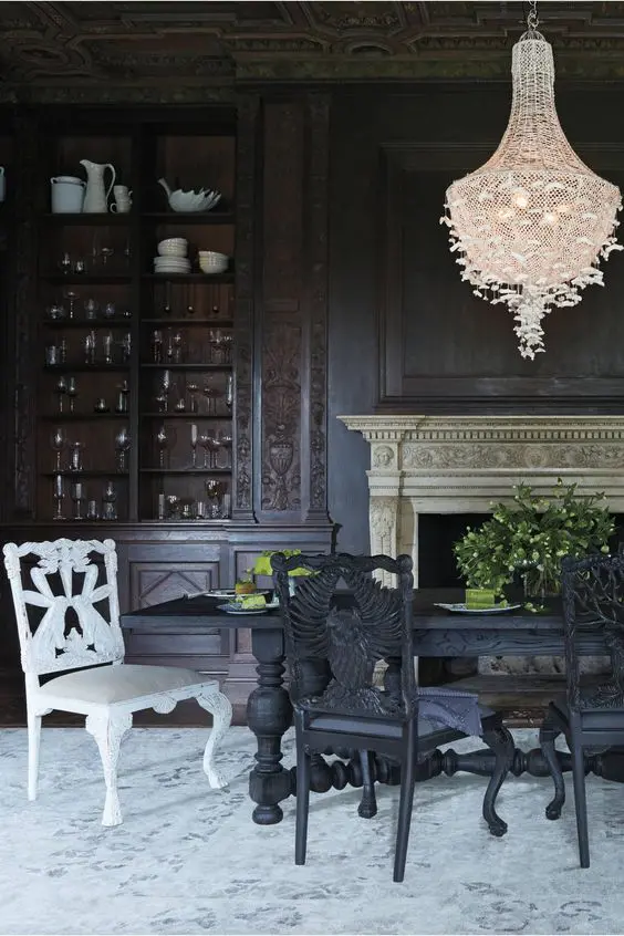 a Gothic dining room with black walls, a black table, black and white chairs, a white butterfly chandelier