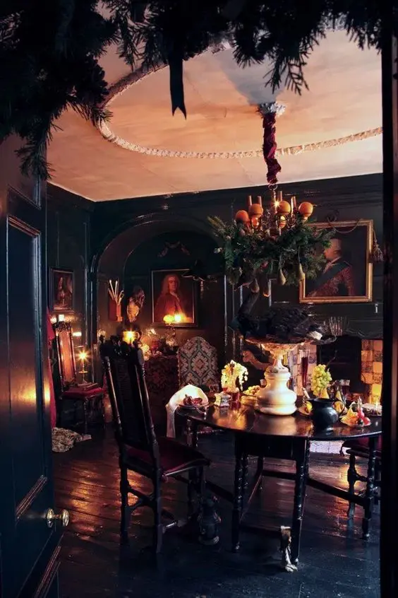 a Gothic dining room with black walls and a floor, a round table, chairs, artworks, candles and a fireplace