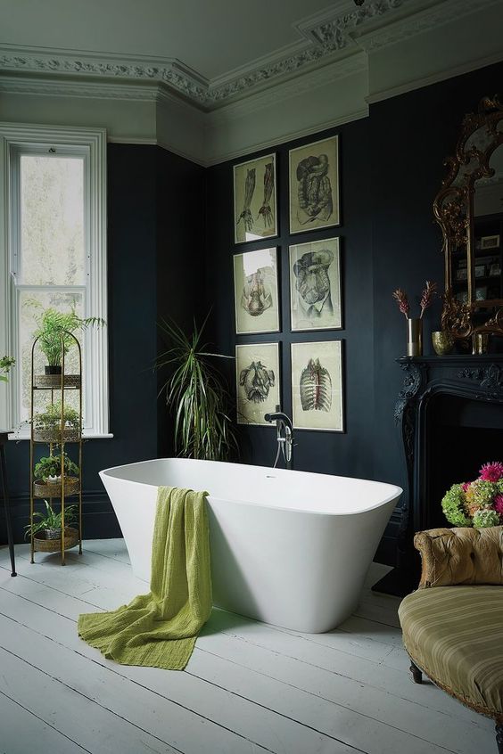 a Victorian Gothic bathroom with black walls and molding on the ceiling, a refined black fireplace, a modern tub, a grid gallery wall and lots of potted plants