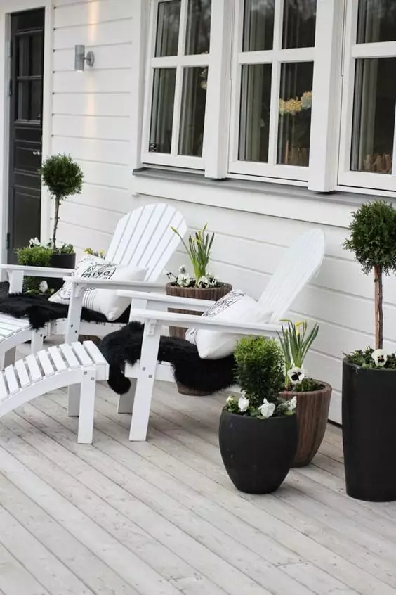 a black and white Scandinavian porch with white loungers, black and white upholstery, potted greenery and blooms