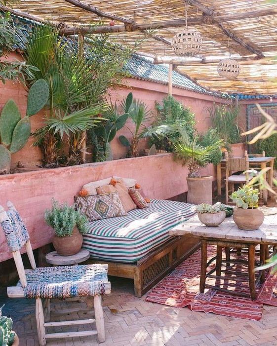 a boho desert terrace done in pink shades, with potted cacti and palm trees, printed linens and a printed rug
