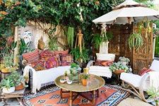 a bright boho terrace with colorful printed textiles, potted greenery, a metal table and carved wooden furniture