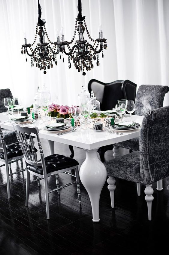 a catchy Gothic dining space with a white table with unique legs, black chairs and armchairs, black crystal chandeliers over the table