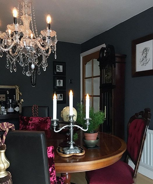 a chic Gothic kitchen with black walls, a round table, burgundy chairs, a crystal chandelier, potted greenery and artworks