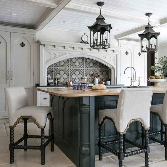 a chic Gothic kitchen with white cabinetry, a graphite grey kitchen island, neutral upholstered stools and catchy vintage lamps