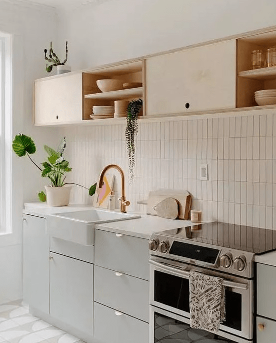 A chic kitchen in dove grey and light colored plywood, with white countertops and a white stacked tile backsplash