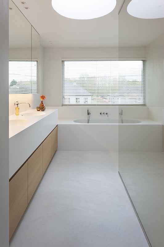 a clean minimalist bathroom with a built-in bathtub, a large vanity and built-in sinks, a large window with shutters