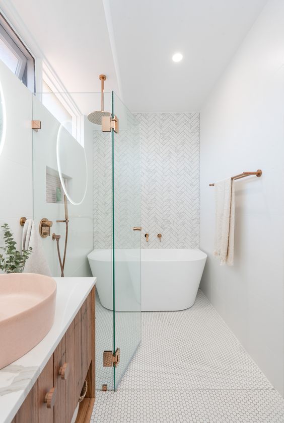 a contemporary bathroom with penny and herringbone tiles, a free-standing tub, a wooden vanity and a pink sink and brass touches