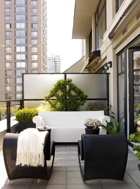 a contemporary monochromatic terrace with black wicker chairs, a white sofa, lots of potted greenery