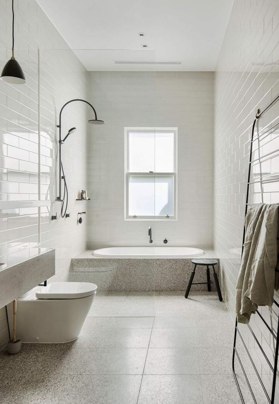 a contemporary neutral bathroom with mismatching tiles, a bathtub clad with stone and white appliances plus black touches
