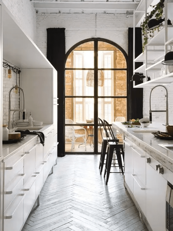 a contrasting galley kitchen with metal cabinets, an arched window, a dining zone by the window and greenery