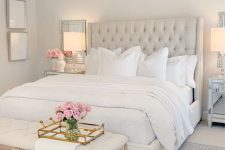 a glam and vintage neutral bedroom with a creay bed, a crystal chandelier, a neutral bench, mirrors and artworks