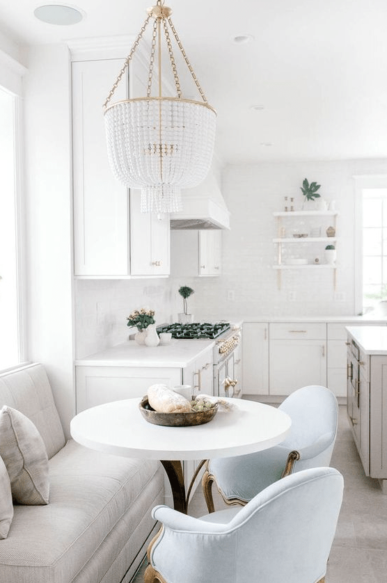 a glam white farmhouse kitchen with a grey kitchen island and a dining zone with a loveseat and blue chairs