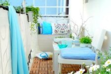 a lovely summer balcony with neutral furniture, blue and printed textiles, an umbrella and some potted greenery and blooms