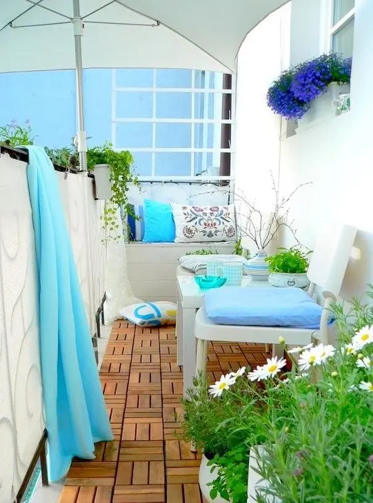 a lovely summer balcony with neutral furniture, blue and printed textiles, an umbrella and some potted greenery and blooms