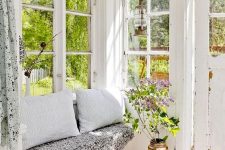 a lovely vintage Scandinavian sunroom in white, with a built-in bench with pillows and faux fur, blooms and greenery in a tall vase is cozy