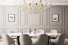 a luxurious dining space with a grye paneled wall, a large beautiful chandelier, a long oval table and grey upholstered chairs