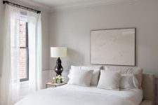 a minimalist neutral bedroom with an upholstered bed, neutral bedding, a retro chandelier and a statement artwork