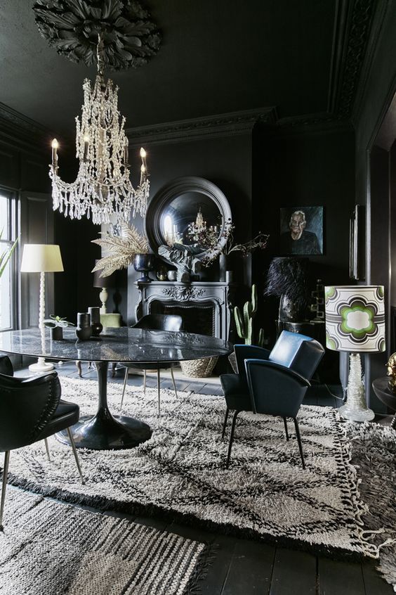 a modern Gothic dining room with black walls, floos and a ceiling, a stone table, leather chairs, mirrors, artworks and a refined chandelier