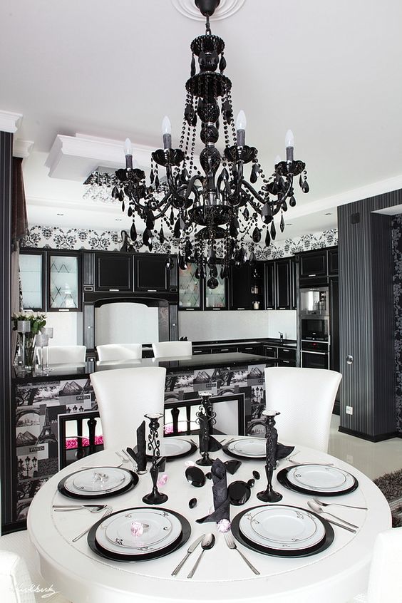a modern Gothic eat-in kitchen with black cabinetry, a print tile kitchen island, a large black crystal chandelier and a white table and chairs