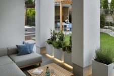 a modern patio with lit up pots with greenery, an L-shaped sofa and a wooden slab table in the center