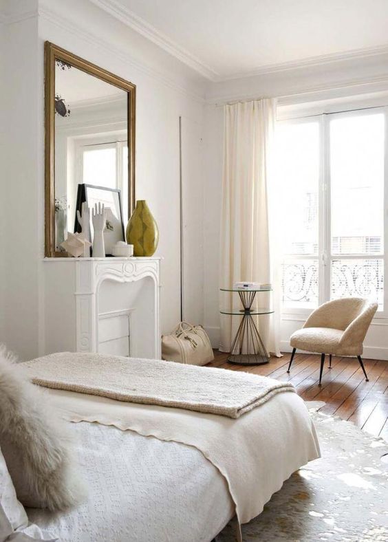 a neutral Parisian bedroom with a non-working fireplace, neutral furniture and linens and pretty artworks