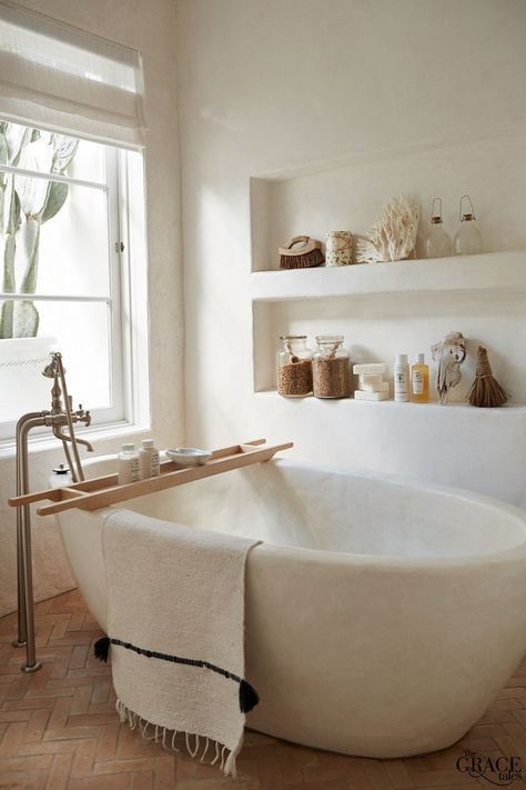 A neutral and welcoming bathroom with built in shelves, an oval tub carved of stone and touches of wood