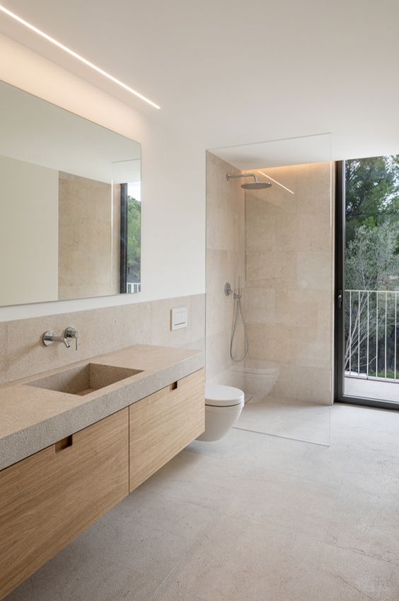 a neutral bathroom with a wooden vanity with a concrete countertop, neutral tiles and a narrow and long window is amazing