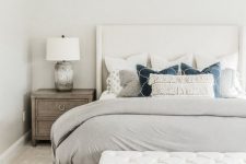 a neutral bedroom with a creamy bed, a white upholstered bench, wooden nightstands and printed pillows