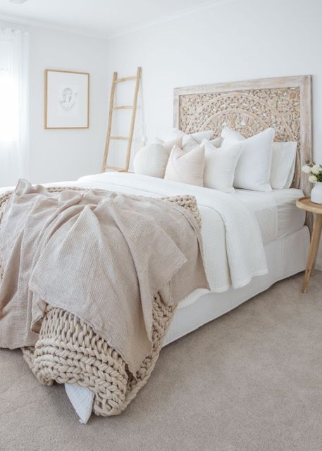a neutral boho bedroom with a carved wooden bed, a ladder, neutral and tan bedding and a wooden nightstand