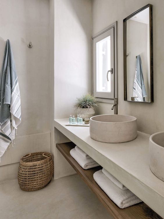 a neutral contemporary bathroom clad with white concrete, with a white concrete vanity and sinks, a basket and neutral textiles