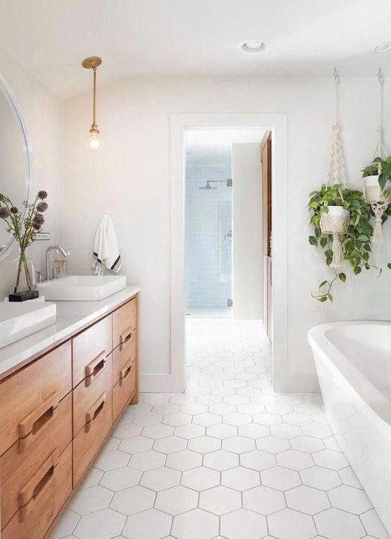 a neutral farmhouse bathroom with large scale hex tile,s a wooden vanity, an oval tub, white sinks and a pendant bulb