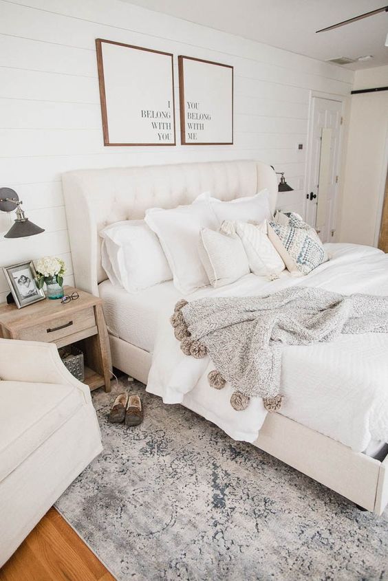 a neutral farmhouse bedroom with creamy furniture, artworks, neutral textiles and printed rugs and blankets