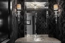 a refined Gothic bathroom with printed wallpaper, chic black furniture, a large mirror and cool crystal lamps and a chandelier