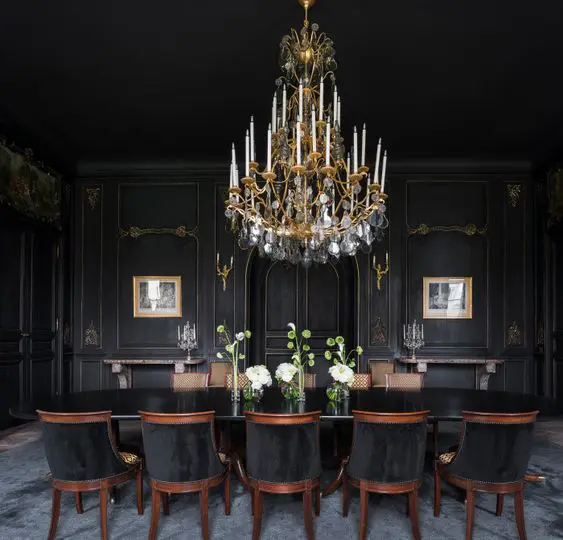 a refined Gothic dining room with black walls, a black table and chairs, artworks and a large crystal and gold chandelier