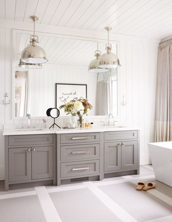 a refined farmhouse bathroom with a grey vanity, a free-standing tub, metal pendant lamps and colro block curtains