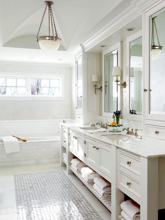 A refined neutral bathroom with a vintage built in vanity, a tub clad with marble tiles, a pendant lamp and mirrors
