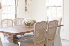 a refined neutral dining room with a stained table, whitewashed chairs with cane backs, a lovely chandelier and much natural light