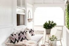 a relaxed Scandinavian porch with a white shabby daybed and white chairs and tables, firewood, greenery and cozy blankets and pillows