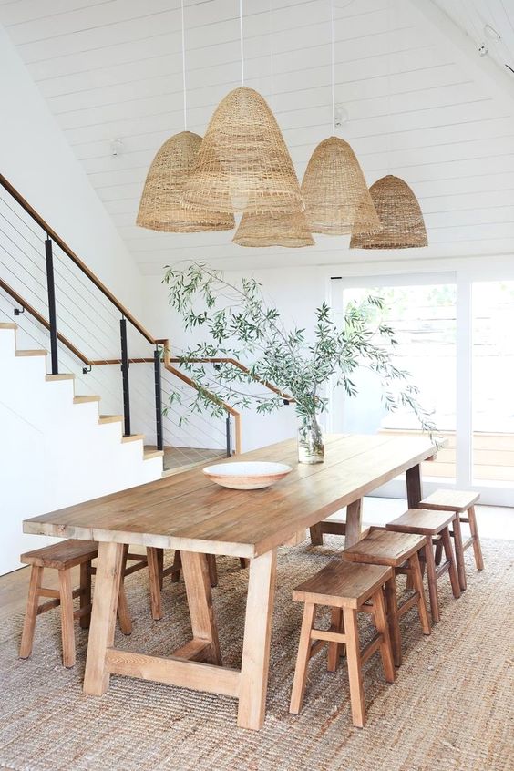 a relaxed boho rustic dining space with a stained dining set with stools, some pendant lamps and greenery on the table