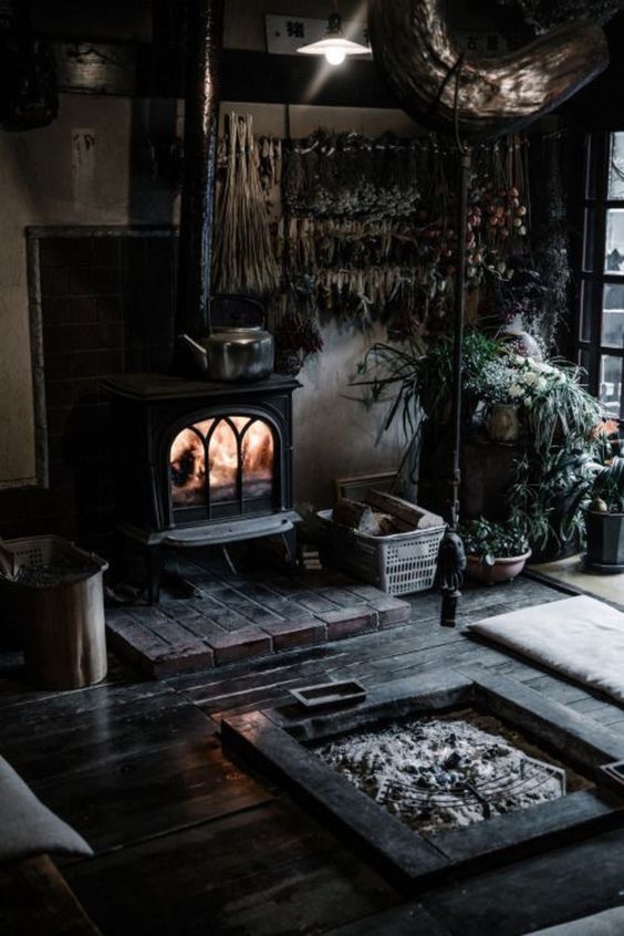 A rustic Gothic space with a vintage hearth, a firepit, potted plants, and black floors for a witch like feel