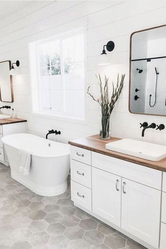 a serene farmhouse bathroom with a white vanity, a wooden countertop, an oval tub, mirrors in sleek frames
