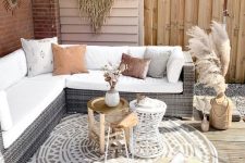 a simple neutral boho terrace with a wicker corner sofa, an arrangement of coffee tables, a dried grass hanging and an umbrella