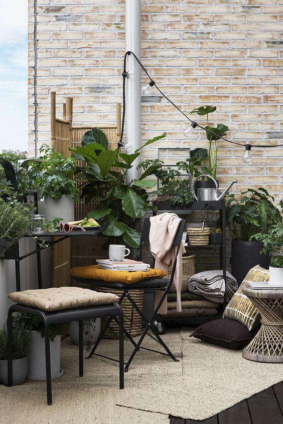 a smal boho terrace with metal furniture, a wooden table, potted greenery, lights and a wooden screen