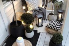 a small Scandinavian balcony with a black egg-shaped chair, candle lanterns and string lights, potted greenery