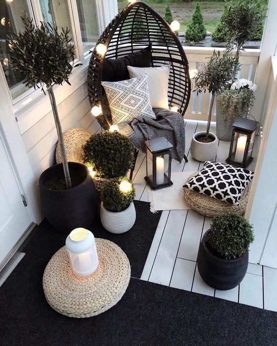 A small Scandinavian balcony with a black egg shaped chair, candle lanterns and string lights, potted greenery