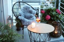 a small and chic balcony with wicker chairs, a round coffee table, potted blooms and plants and candle lanterns