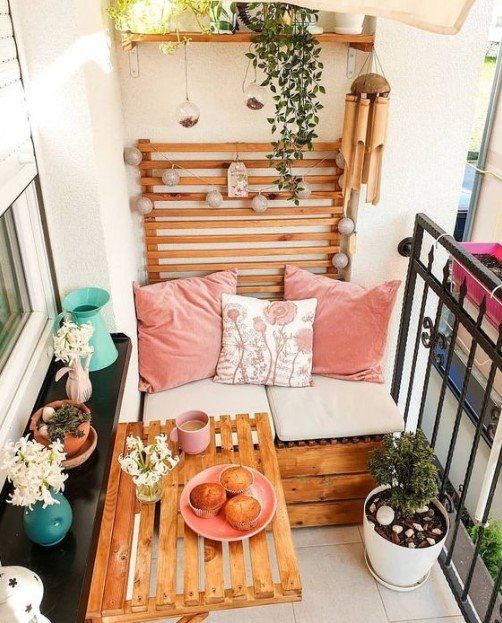 a small and cool balcony with a built-in bench with pillows, a shelf, a folding table, potted plants and blooms and some lights