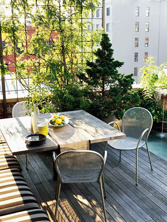 a small and cozy terrace with an upholstered bench, a wooden table, metal chairs and a mini garden in pots