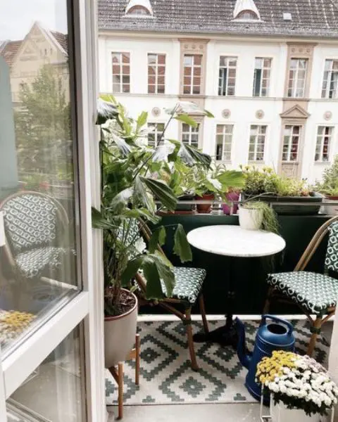 a small boho balcony with a printed rug, a round table, printed chairs, potted blooms and plants is amazing